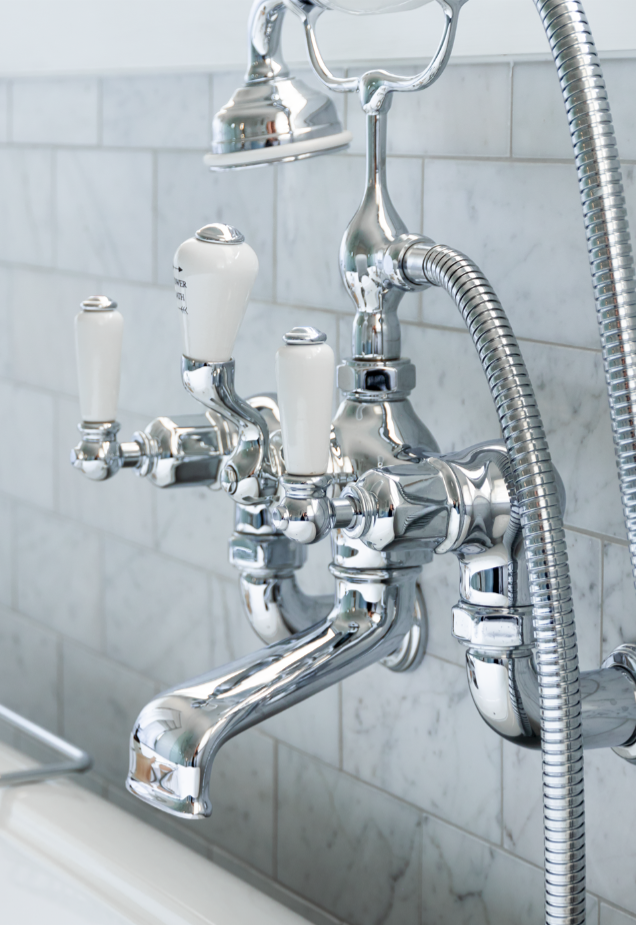 Close up of wall-wounted bath mixer tap in chrome with white ceramic lever handles and diverter lever to operate handshower.